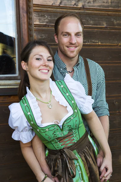 Bavarian couple standing in front of a wooden house — Stock Photo, Image