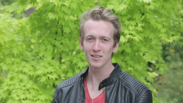 Young blond man in leather jacket standing outside and talking upset into camera — Stock Video