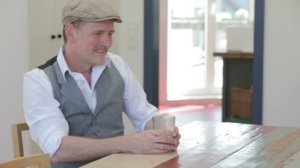 Man sitting at table and drinking coffee and smiles — Stock Video