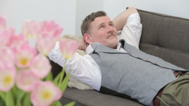 Мужчина лежит на диване и выглядит очень счастливым и довольным — стоковое видео