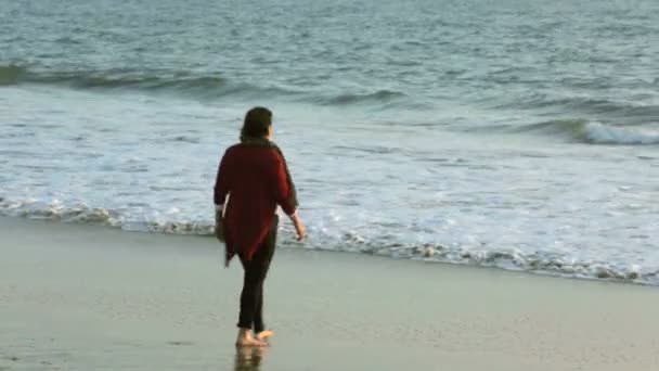 Woman walking along the beach at sunset and stretching her arms — Stock Video