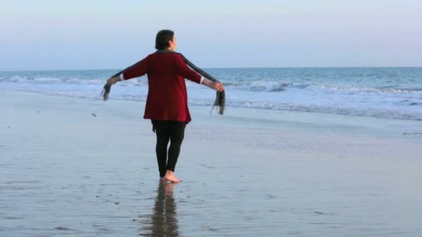 Woman walking along the beach at sunset and stretching her arms — Stock Video