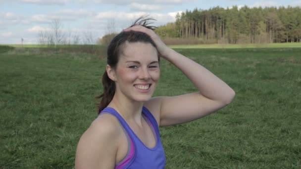Jonge vrouw in de sport versnelling permanent buiten in het gras en glimlachen op camera — Stockvideo