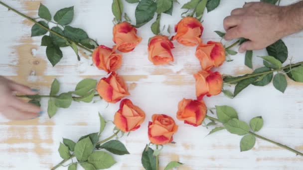 Manos de una mujer y un hombre agarrando rosas que yacen sobre una mesa de madera en forma de corazón — Vídeos de Stock