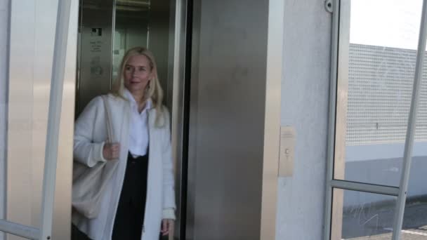 Blond woman walking out of an elevator and looking for someone — Stock Video