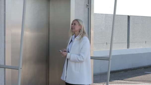 Blond kobieta SMS-y na jej telefon podczas oczekiwania na windę i chodzenie w — Wideo stockowe