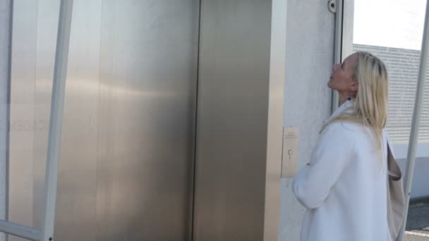 Mujer rubia esperando delante de un ascensor y entrando — Vídeos de Stock