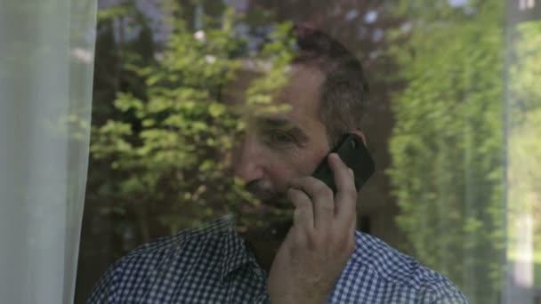 Man standing behind a window and talking on his phone — Stock Video