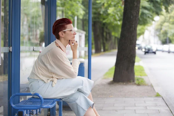 Kvinna sitter vid busshållplatsen och väntar på — Stockfoto