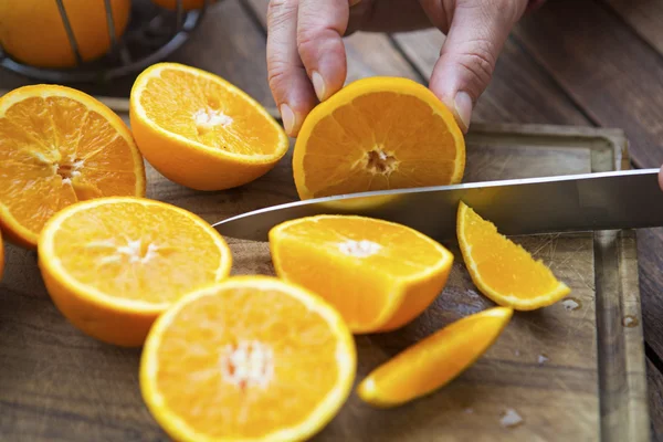 Snij de sinaasappelen met mes op tafel — Stockfoto