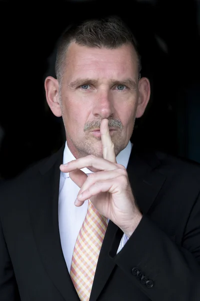 Portrait of businessman holding finger to his mouth — Stock Photo, Image