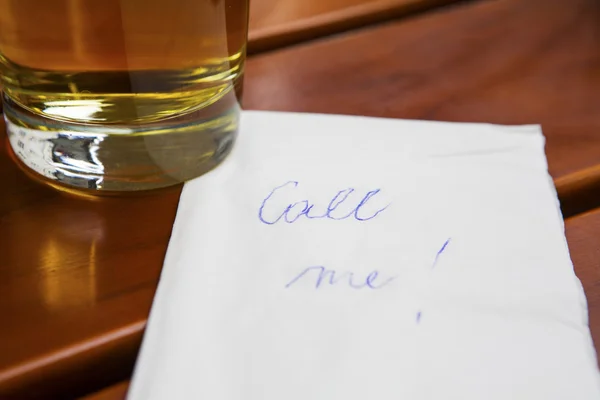 Note "call me" next to a glass of beer — стоковое фото