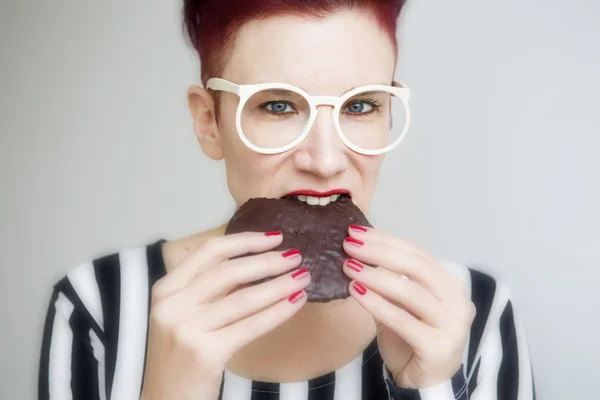 Red-haired woman eating a big chocolate cookie — Stock Photo, Image