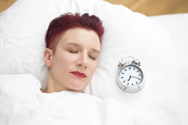 Woman lying in bed with alarm clock on pillow — Stock Photo, Image