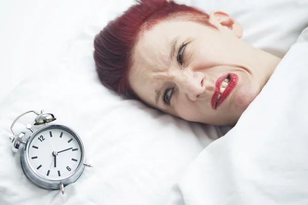 Angry woman lying in bed with alarm clock on pillow — Stock Photo, Image