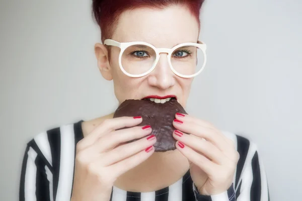 Roodharige vrouw eten een grote chocolade cookie Rechtenvrije Stockafbeeldingen