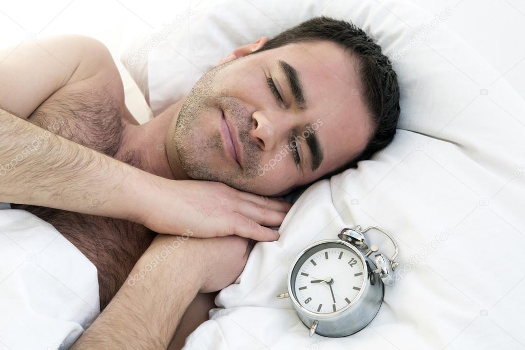 man sleeping in bed with alarm clock