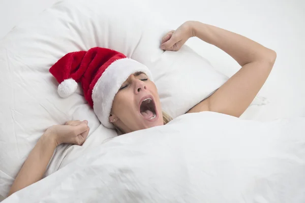 Frau gähnt mit Weihnachtsmütze im Bett — Stockfoto