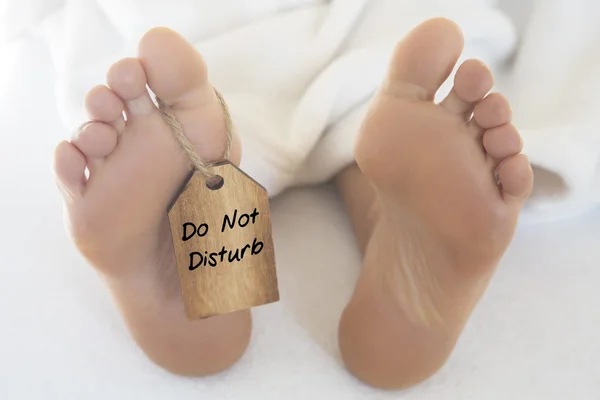 Naked feet  with wooden tag 'do not disturb" — Stock Photo, Image