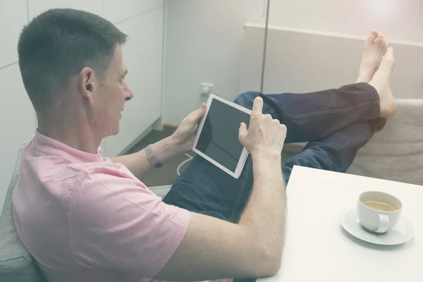 Uomo seduto a tavola con caffè e tablet — Foto Stock