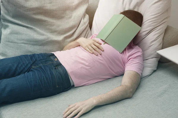 Ember alszik a kanapén könyv a fejét — Stock Fotó