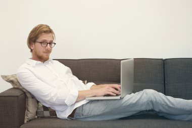 dizüstü bilgisayar ile kanepede oturan genç adam