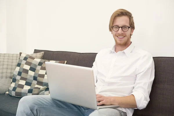 Ung man sitter på soffan med laptop och leenden — Stockfoto