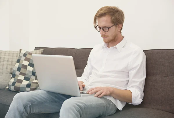 Молодой человек сидит на диване с ноутбуком — стоковое фото