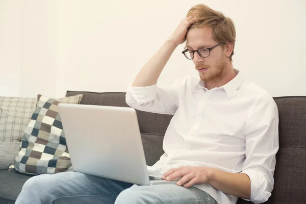 Young man sitting on couch with laptop — Stock Photo, Image
