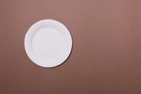 white eco-friendly paper plate on brown colored paper background with copy space. top view. mock-up.