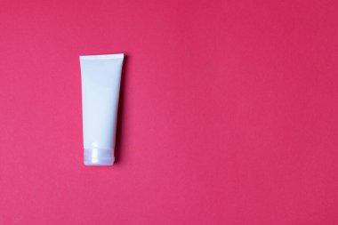 Kırmızı arkaplanda kremalı tüp ve kopyalama alanı.