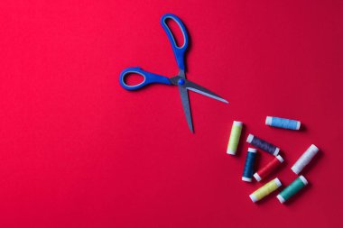 Kırmızı zemin üzerinde makas ve iplik makarası, kopyalama alanı ile.