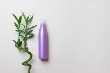 Bambunun yanında duran opak kozmetik şişe açık sarı arkaplanda kopya alanı ile birlikte..