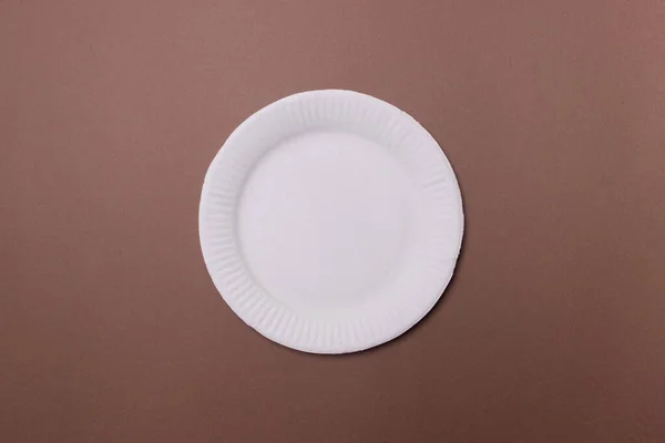 white eco-friendly paper plate on brown colored paper background. top view. mock-up.