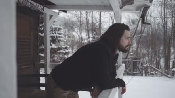 Όμορφος νεαρός άνδρας στο μαύρο πουλόβερ στέκεται πάνω από την ξύλινη βεράντα. — Αρχείο Βίντεο