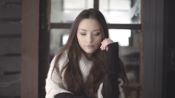 Beautiful young brunette woman wearing knitted sweater sitting on a porch. — Stock Video