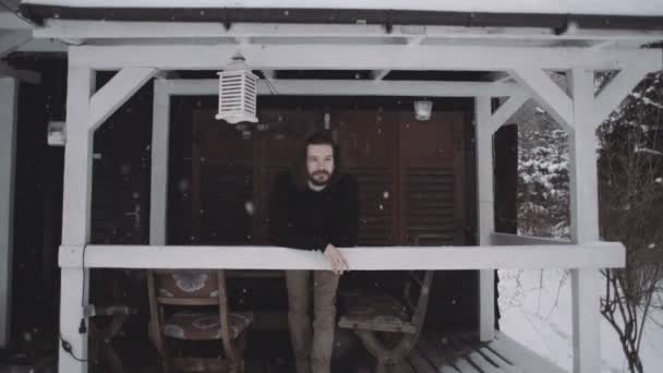 Όμορφος νεαρός άνδρας στο μαύρο πουλόβερ στέκεται πάνω από την ξύλινη βεράντα. — Αρχείο Βίντεο