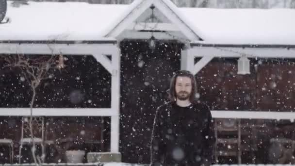 Handsome young man in black sweater standing near an old wooden house. — Stock Video