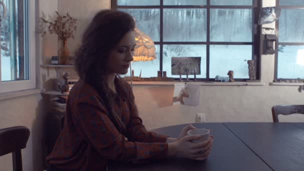 Young woman sitting by a table with cup of tea. — Stock Video