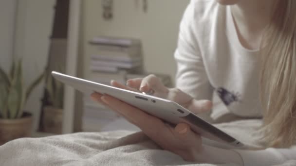 Дівчина лежить на ліжку вдома, використовуючи планшет, в приміщенні . — стокове відео