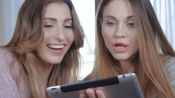Fröhliche Mädchen, die auf dem Bett sitzen und am Tablet chatten. — Stockvideo