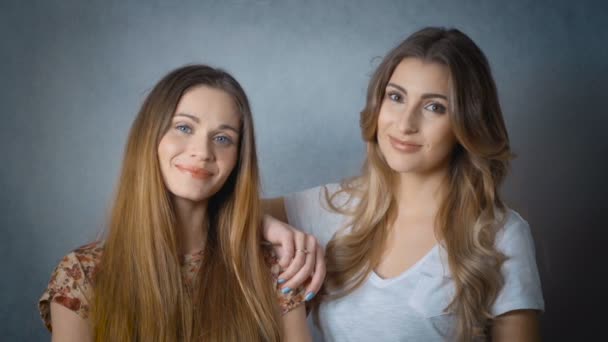 Портрет двух красивых девушек, улыбающихся и смотрящих в камеру в студии . — стоковое видео
