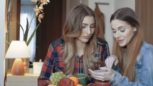 Due giovani amiche sedute accanto a un tavolo e usando il telefono . — Video Stock