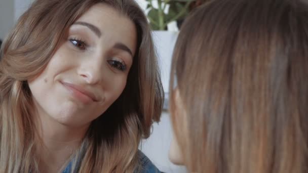 Two young female friends sitting on sofa in the living room and gossiping. — Stock Video