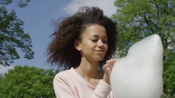 Hermosa mujer afro con hilo dental de caramelo en el soleado parque . — Vídeo de stock