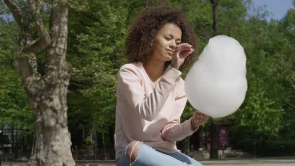 Mooie afro vrouw met candy floss in zonnig park. — Stockvideo