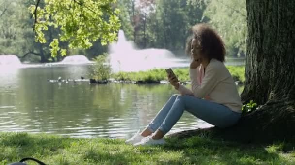Beautiful young girl with dark curly hair using her cell phone, outdoor. — Stock Video