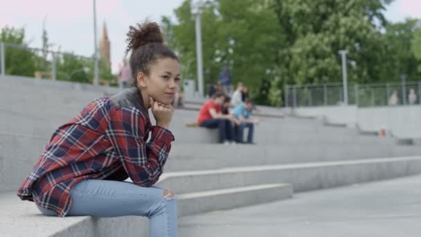 Jonge afro Amerikaanse vrouw zitten in de stedelijke achtergrond. — Stockvideo