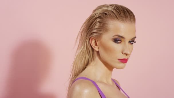 Vacker blond ung kvinna poserar i bikini över rosa bakgrund. — Stockvideo