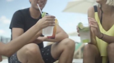 Genç neşeli grup arkadaşıyla sahilde gülüyor, söz ve ahşap koltuğa otururken soğuk içecekler içme - birlikte eğleniyor. 